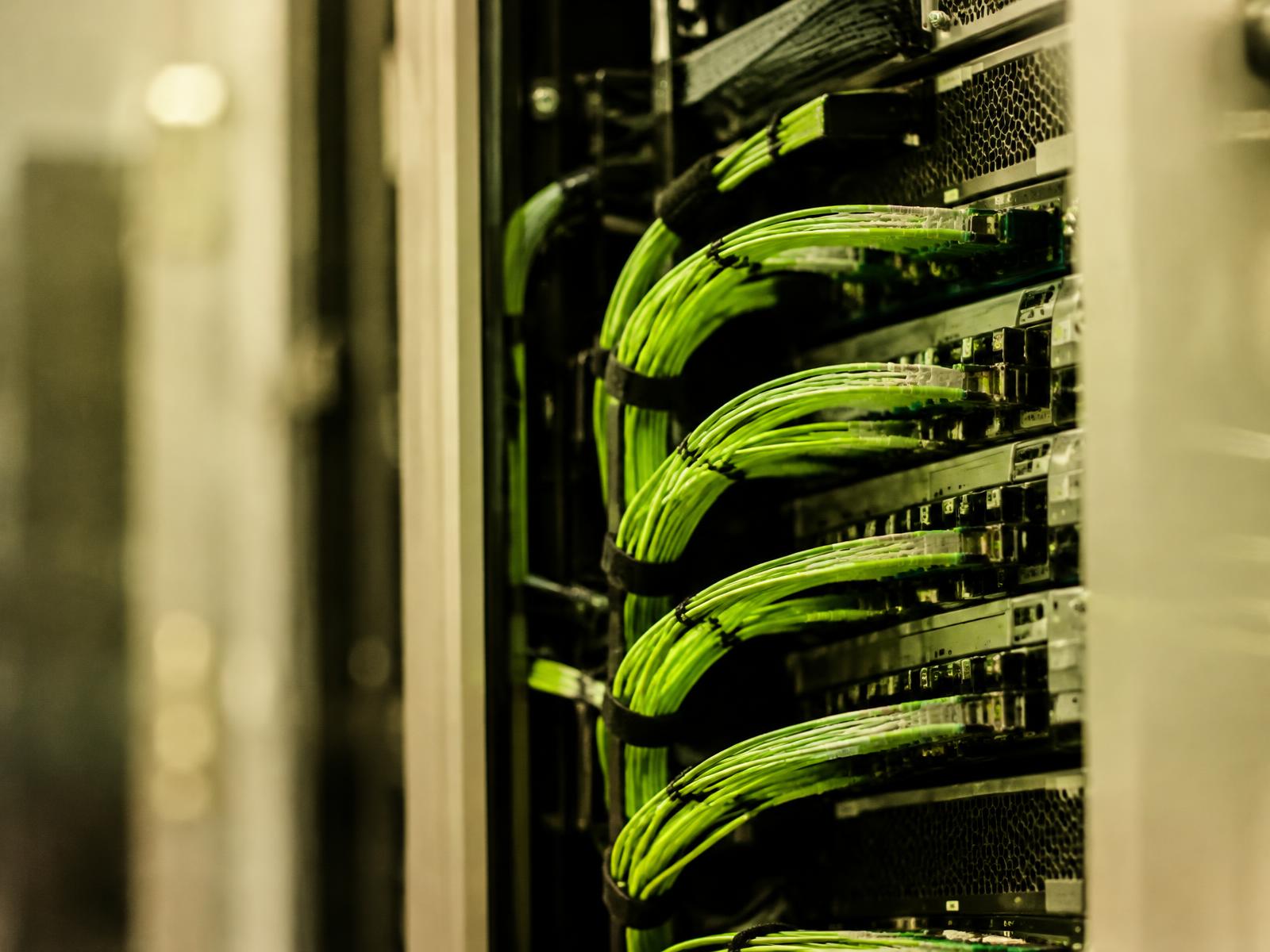 Server rack with bundled lime-green fibre optic cables connected to network switches